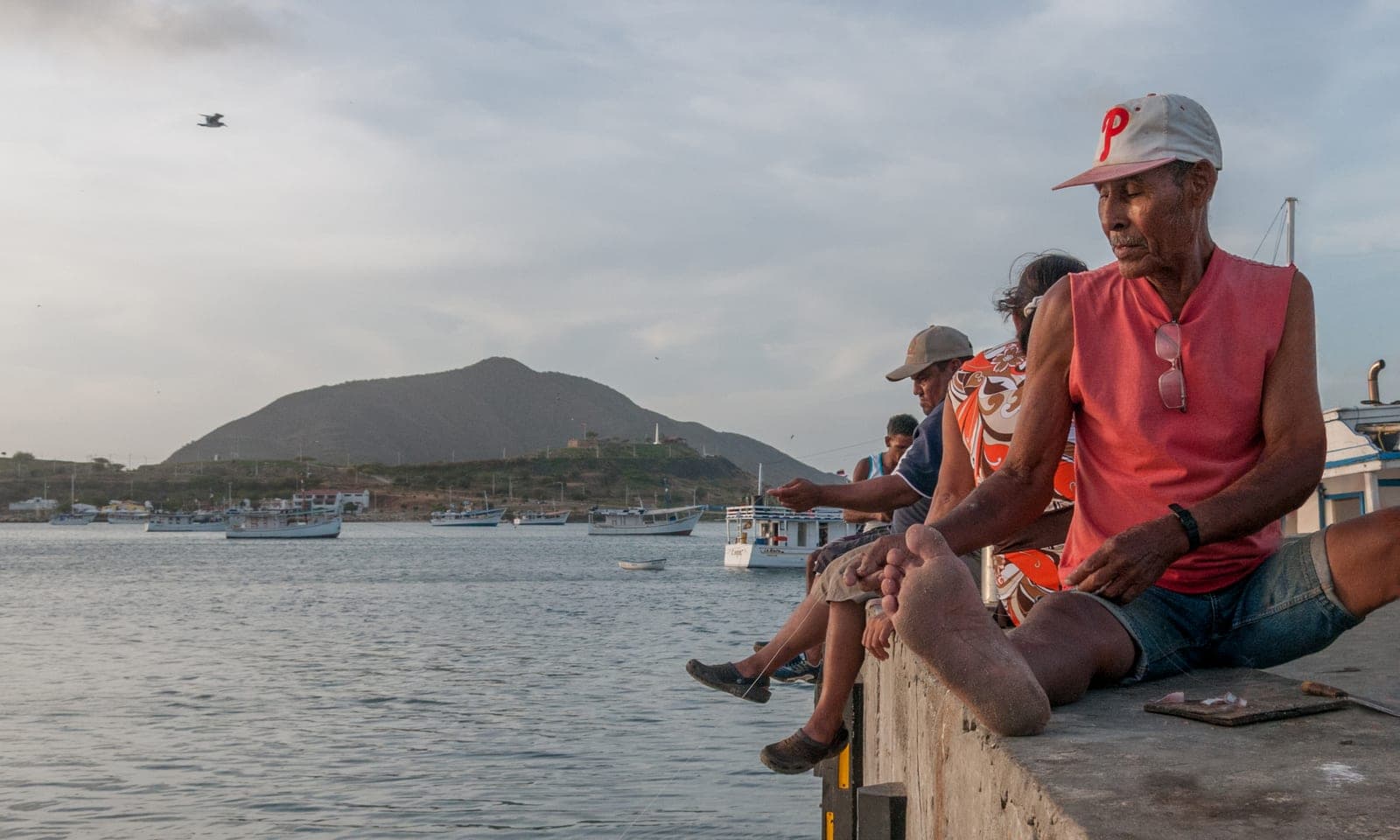 Pescadores sentados en el muelle de Juan Griego, en el norte de Margarita, con lanchas fondeadas en la bahía y un cerro al fondo